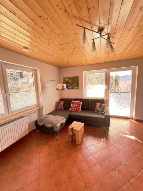 Wohnbereich mit Sofa, Holzdecke, Fenster und einem kleinen Tisch in einem hellen Raum.