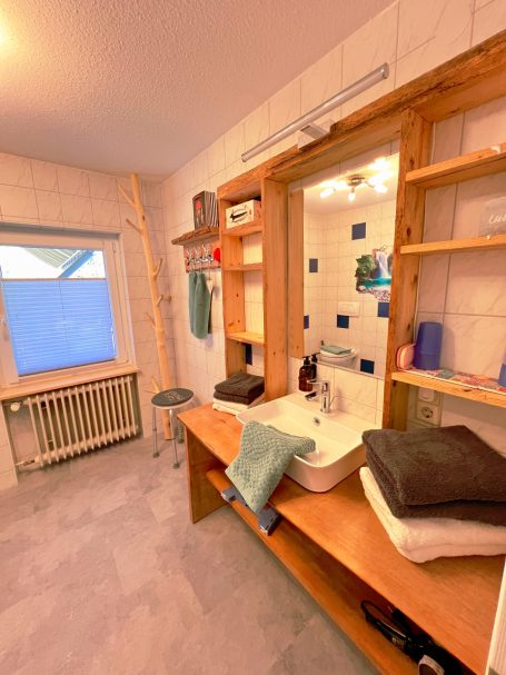 Modernes Badezimmer mit Waschbecken, Spiegel und Regalen, helle Farben und Fenster Licht.