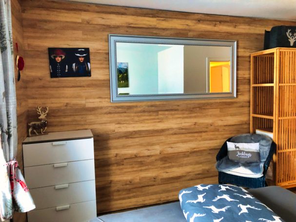 Schlafzimmer mit Holzwand, Spiegel, Kommode und Regal. Moderne, gemütliche Einrichtung.