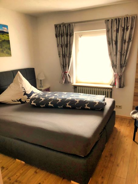 Helle Schlafzimmereinrichtung mit Bett, Kissen und Vorhängen in neutralen Farben.