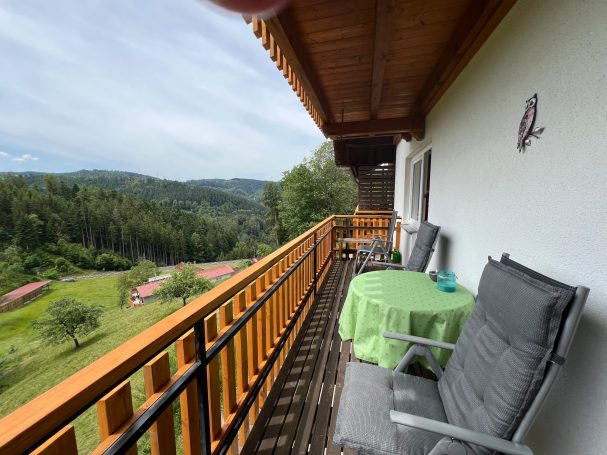 Balkon mit Aussicht auf grüne Hügel und Möbel im Freien.