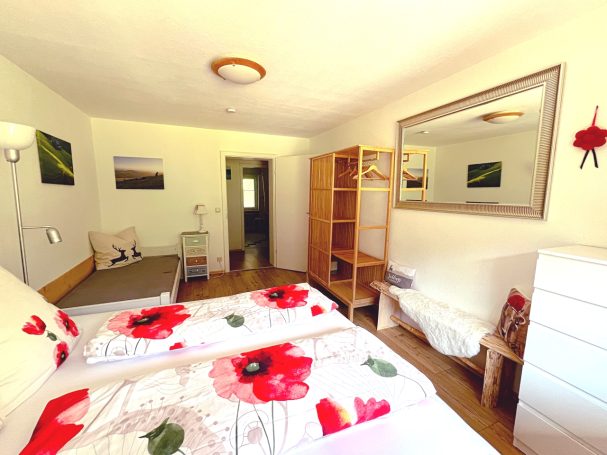 Helles Schlafzimmer mit zwei Betten, Holzmöbeln und offenem Kleiderschrank