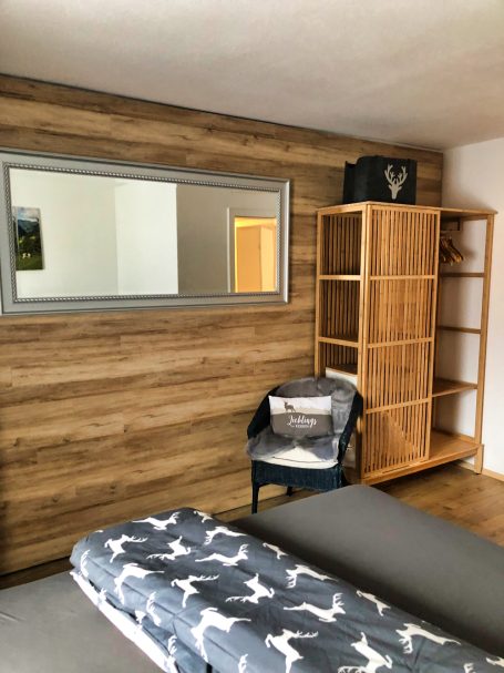 Heller Raum mit Holzwänden, einem Spiegel, einem Regal und einem Stuhl.