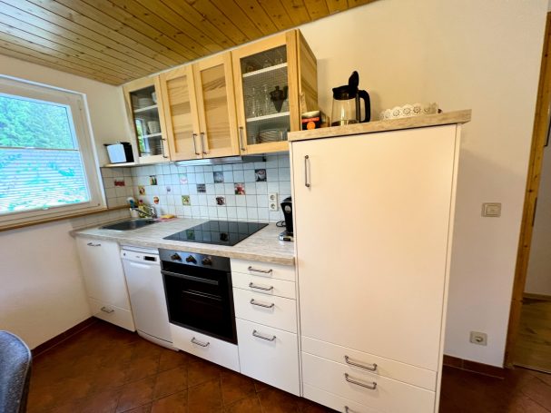 Moderne Küche mit Herd, Kühlschrank und Holzregalen, helle Wände und Fenster.
