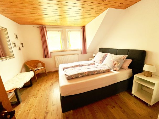 Helle Schlafzimmer mit Doppelbett, Holzfußboden und Fenster mit Vorhängen.