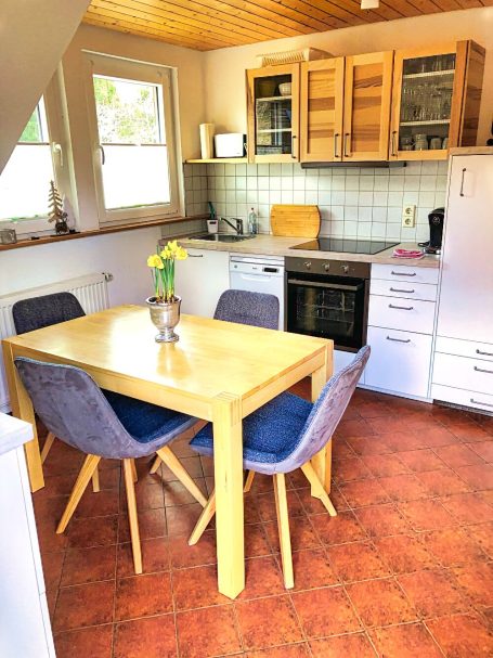 Kleine Küchenzeile mit Tisch, Stühlen, Kühlschrank und Backofen in hellen Farben.