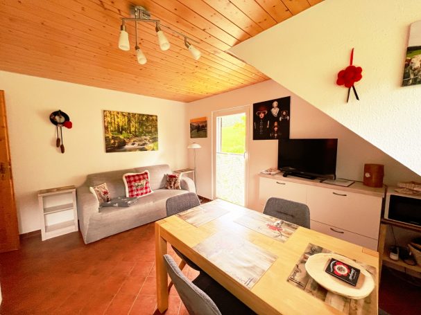 Helles Wohnzimmer mit Sofa, Esstisch und Fernseher, Zugang zur Terrasse. 